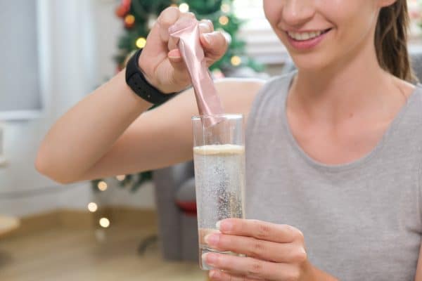Young Caucasian Woman Preparing Healthy Supplement After Exercise Dissolving Collageen Powder In Glass Of Water.