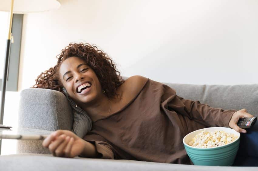 Laughing Woman On Sofa With Tv Remote And Popcorn. Niets doen