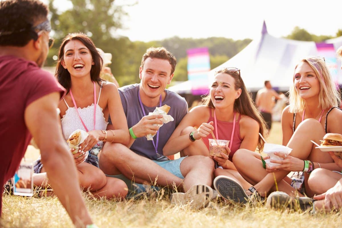 Friends Sitting On Grass And Eating At Music Festival
