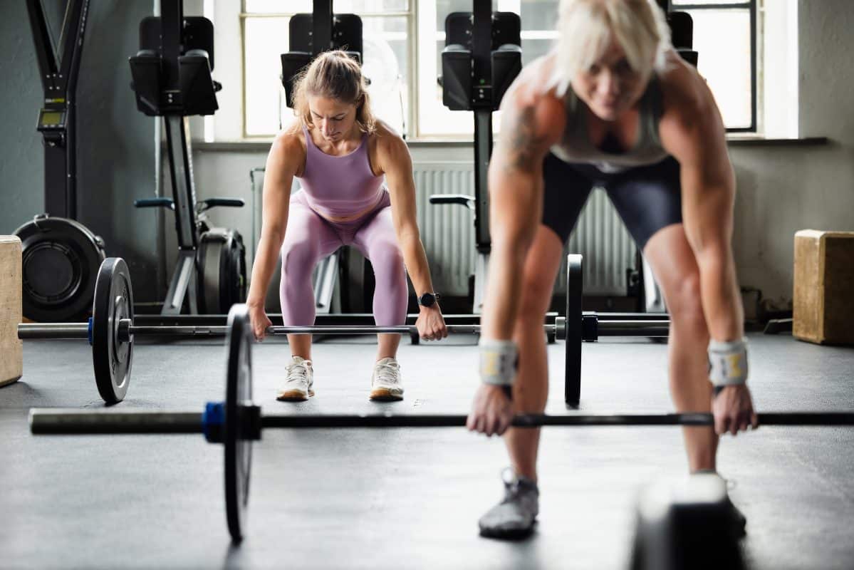 Female Cross Training Athletes Preparing For Deadlift Exercise In Gym