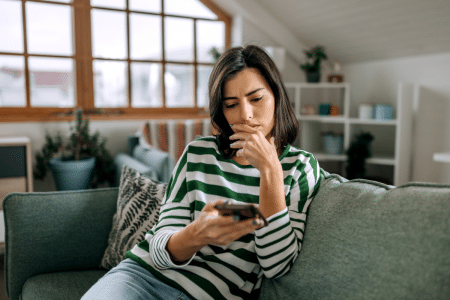 Vrouw zit op bank en kijkt naar telefoon