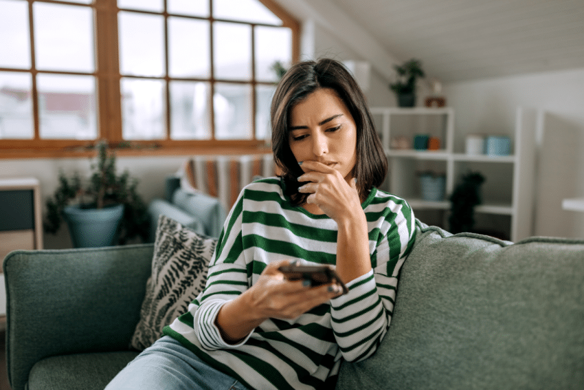 Vrouw zit op bank en kijkt naar telefoon