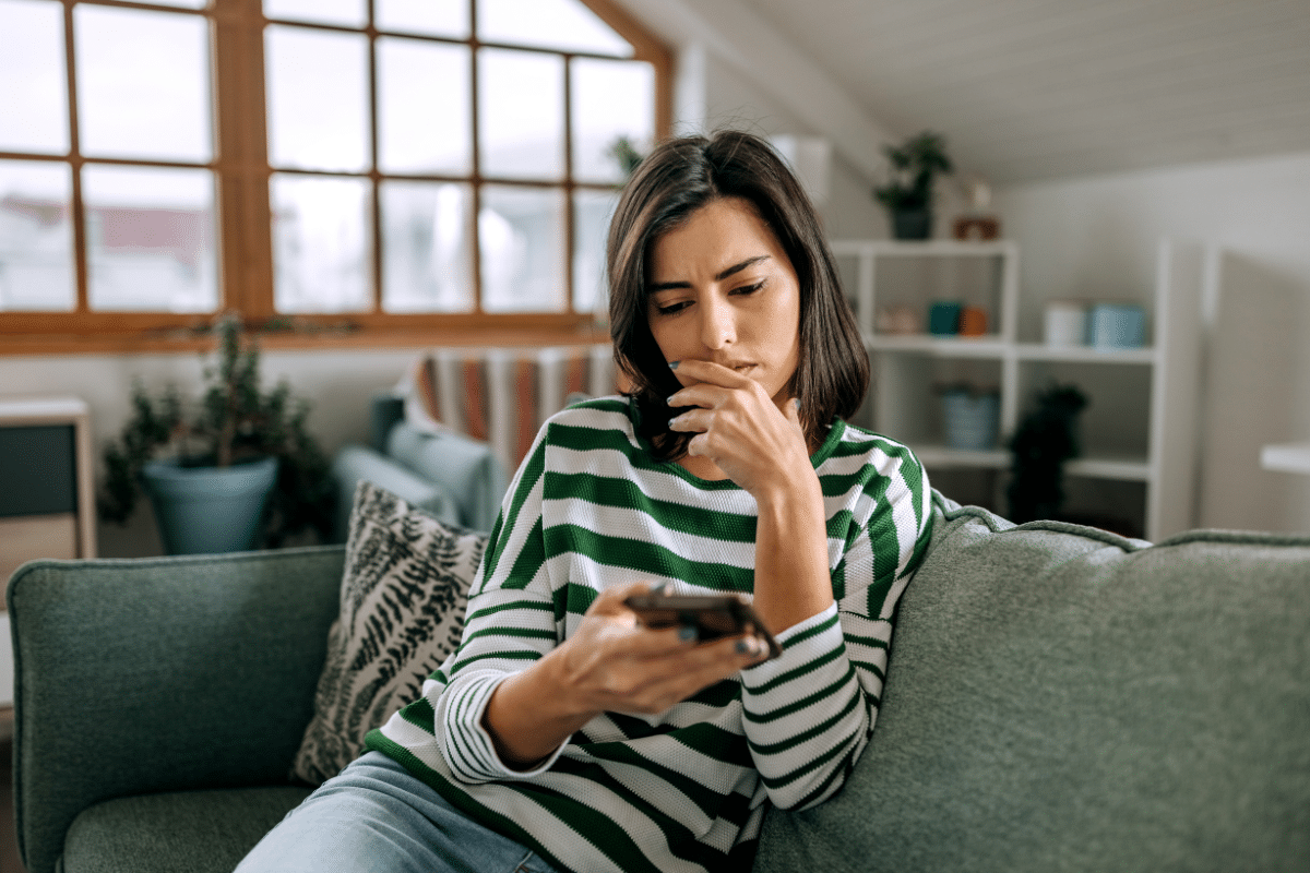 Vrouw zit op bank en kijkt naar telefoon