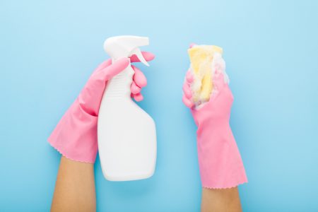 Hands In Rubber Protective Gloves Holding White Spray Bottle And Foamy Sponge. Detergent For Different Surfaces In Kitchen, Bathroom And Other Rooms. Pastel Blue Background. Point Of View Shot.